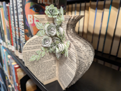 Picture of book cut into shape of a vase with some paper scrapbook flowrs.