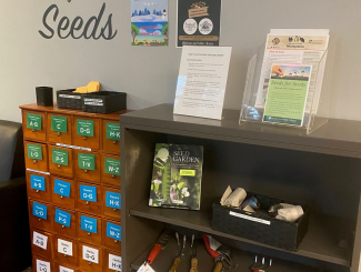 Picture of the seed library and adjoining bookshelf with handouts and garden tools for checkout